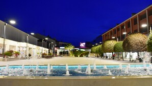 Vue nocturne d’une place publique avec une fontaine centrale, entourée de bâtiments à l’architecture moderne et dotée d’espaces de détente en plein air.