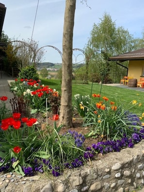Een tuin met verschillende bloemen, een stenen muur en een gebouw met een geel dak.