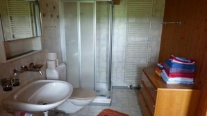 Une salle de bain équipée d’une douche, de toilettes, d’un lavabo et d’un meuble en bois contenant des serviettes.