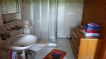 A bathroom with a shower, toilet, sink, and a wooden cabinet with towels.
