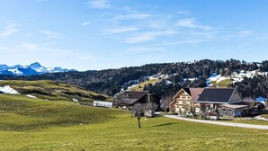 Un paysage rural avec un bâtiment doté d’un toit en pente, d’un petit porche et d’un garage apparent.