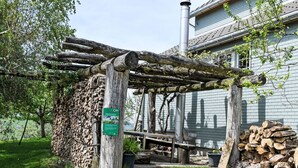 Un espace extérieur rustique agrémenté d’une pergola en bois, d’une pile de bois de chauffage et d’une cheminée.