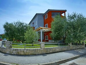 Un bâtiment moderne à deux étages, doté d’une façade rouge et grise, d’un patio couvert et d’un mur de soutènement en pierre.