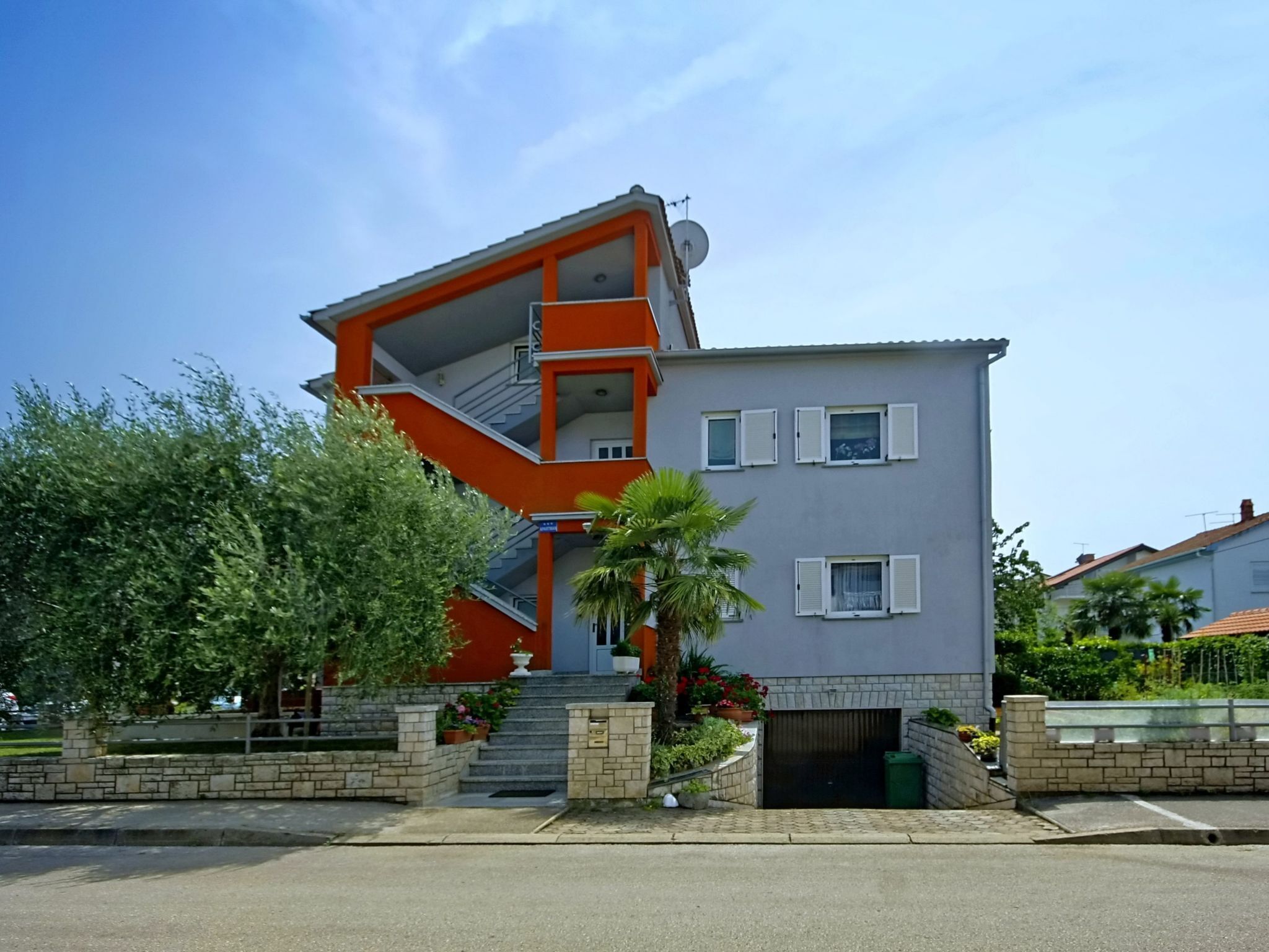 En modern byggnad i två våningar med en unik, kantig design, som utmärks av en iögonfallande orange trappa och en liten trädgårdsdel med palmer och krukväxter.