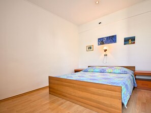 A bedroom with a wooden bed, a nightstand, a wall-mounted lamp, and two framed pictures. - Apartment Nika 5 in der Residenz mit Pool und Whirlpool in Strandnähe by Interhome (Umag)