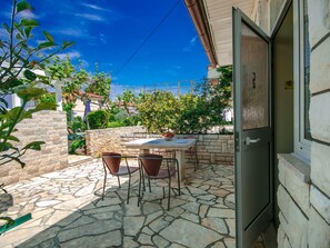 A stone patio with a table and chairs, a stone wall, and a door leading to a room. - Apartment Nika 5 in der Residenz mit Pool und Whirlpool in Strandnähe by Interhome (Umag)
