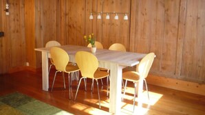 Un comedor con mesa y sillas de madera, un jarrón con flores e iluminación colgante.