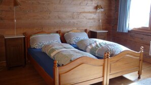 Una cama con estructura de madera, dos almohadas y una colcha azul en una habitación con paredes de madera y una ventana con cortinas.