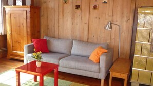 Una sala de estar acogedora con un sofá gris, cojines rojo y naranja, una mesa de centro de madera y una mesita auxiliar.