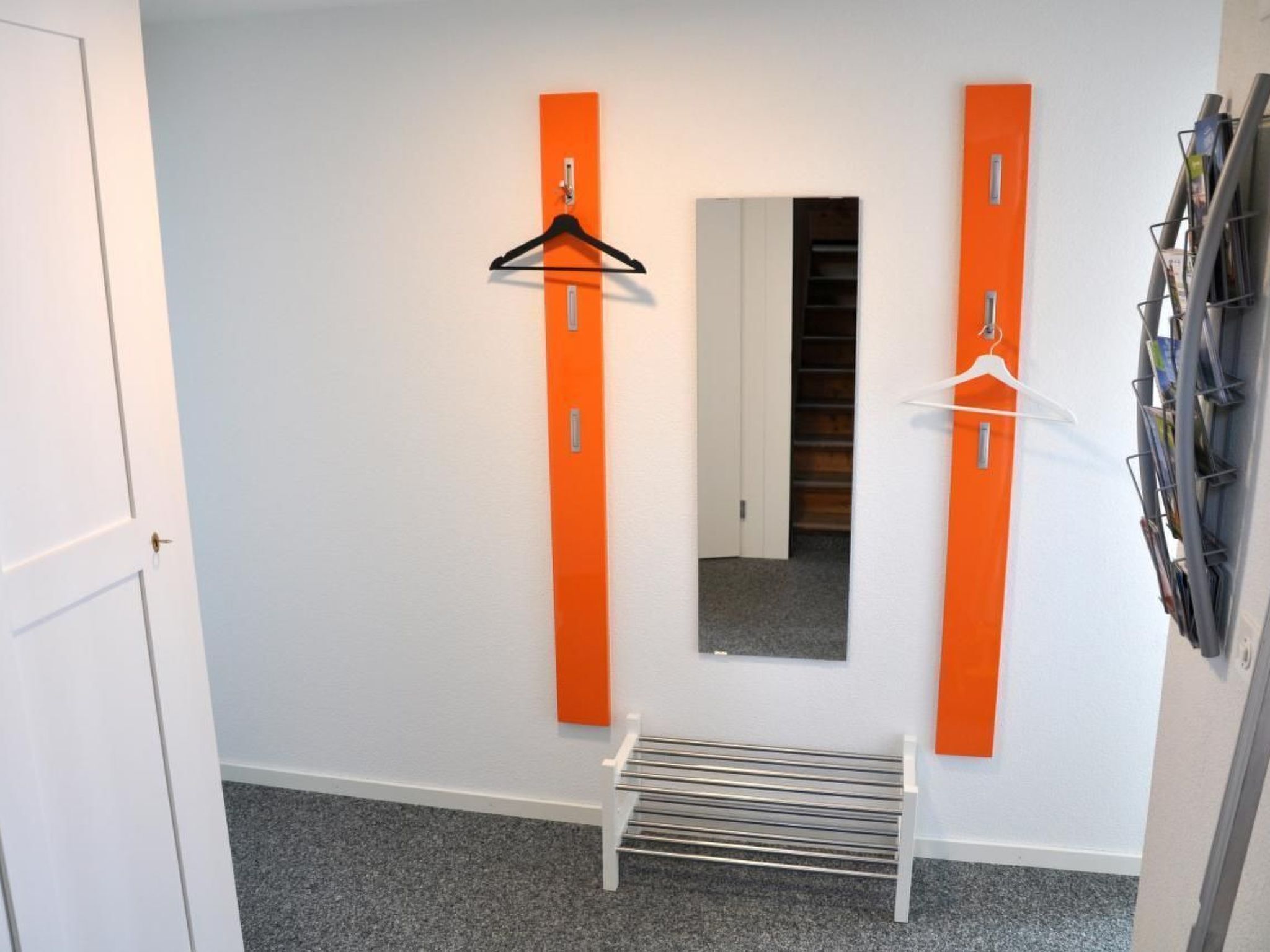 A hallway with a bench, two orange vertical elements, a mirror, and a rack of magazines.