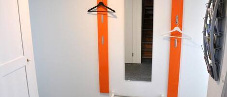 A hallway with a bench, two orange vertical elements, a mirror, and a rack of magazines.