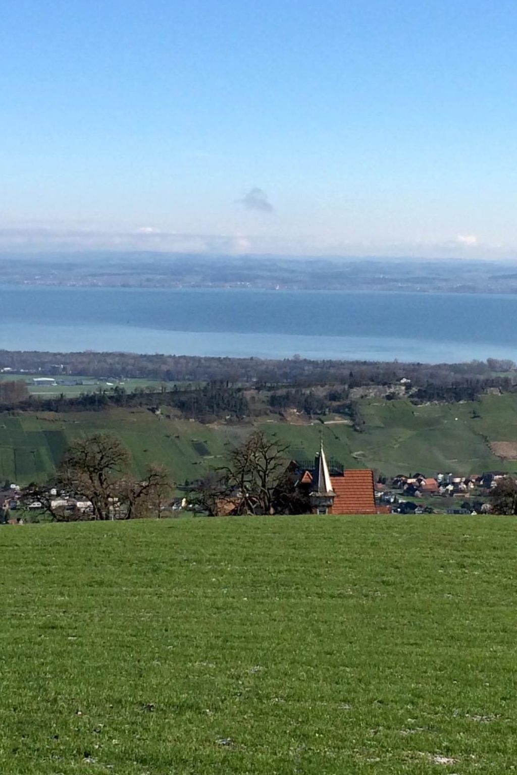 Uitzicht op een kustlandschap met een kerk en huizen op de voorgrond, en een groot wateroppervlak in de verte.