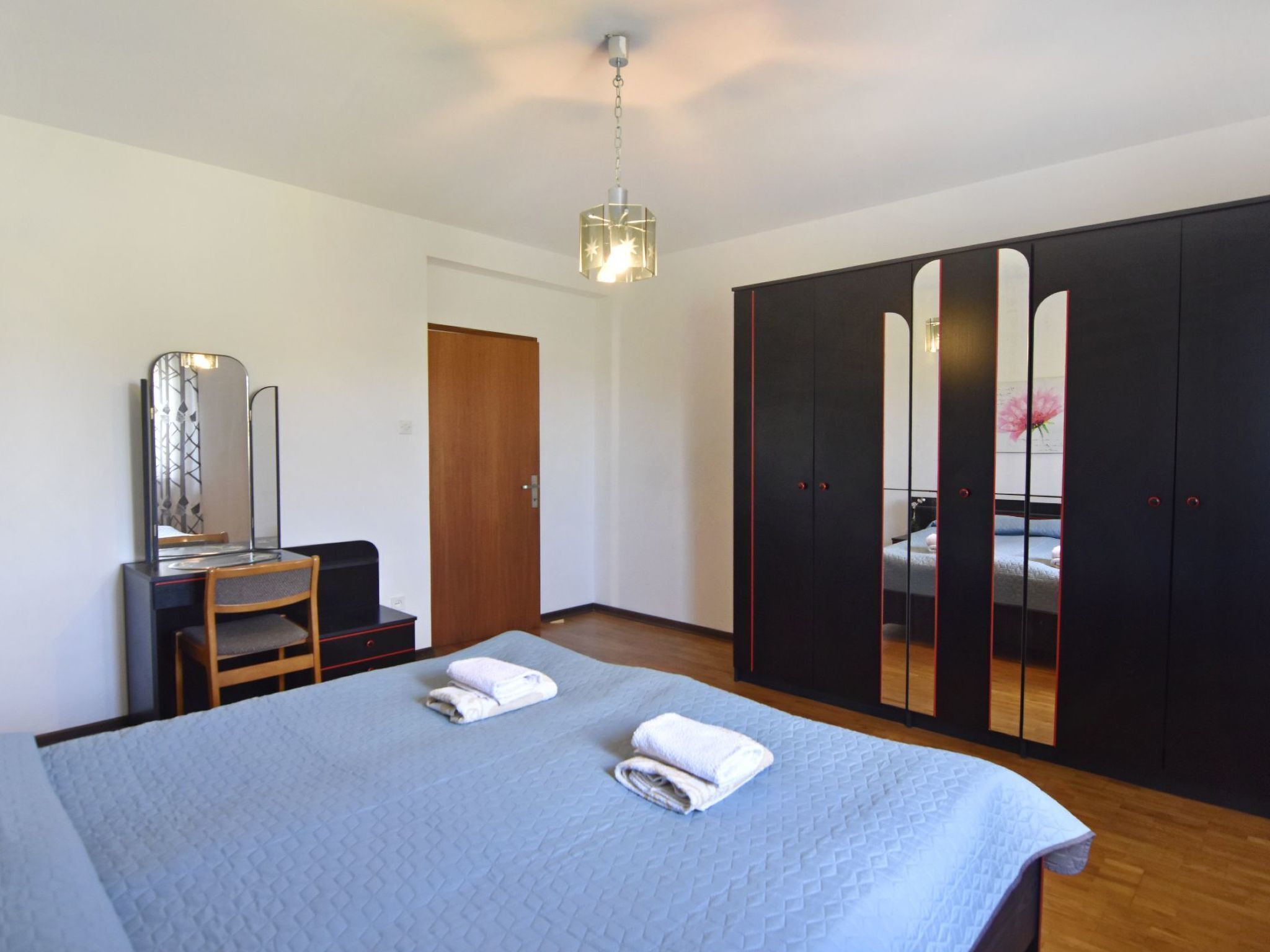 A bedroom with a bed, a desk with a chair, a wardrobe, and a mirror.