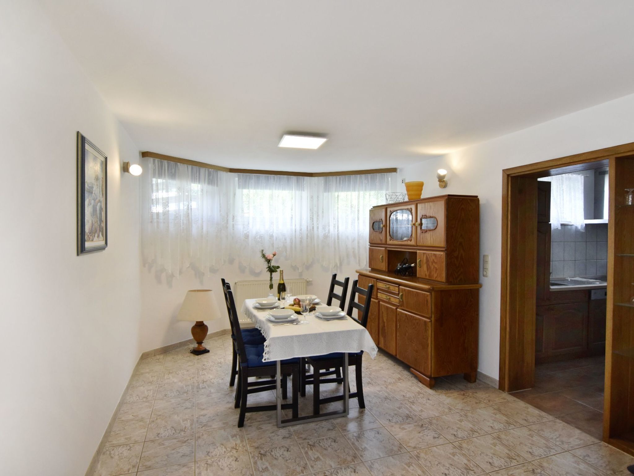 A dining area with a table set for four, a wooden cabinet, and a kitchen visible through an open door.