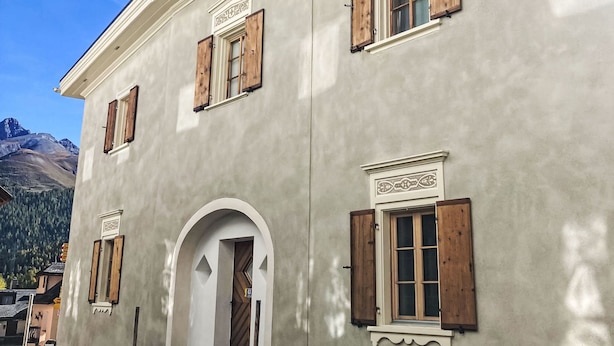 A building with wooden shutters, a white door, and a mountain backdrop. - Chesa alb sco'l floc by Interhome (S-chanf)