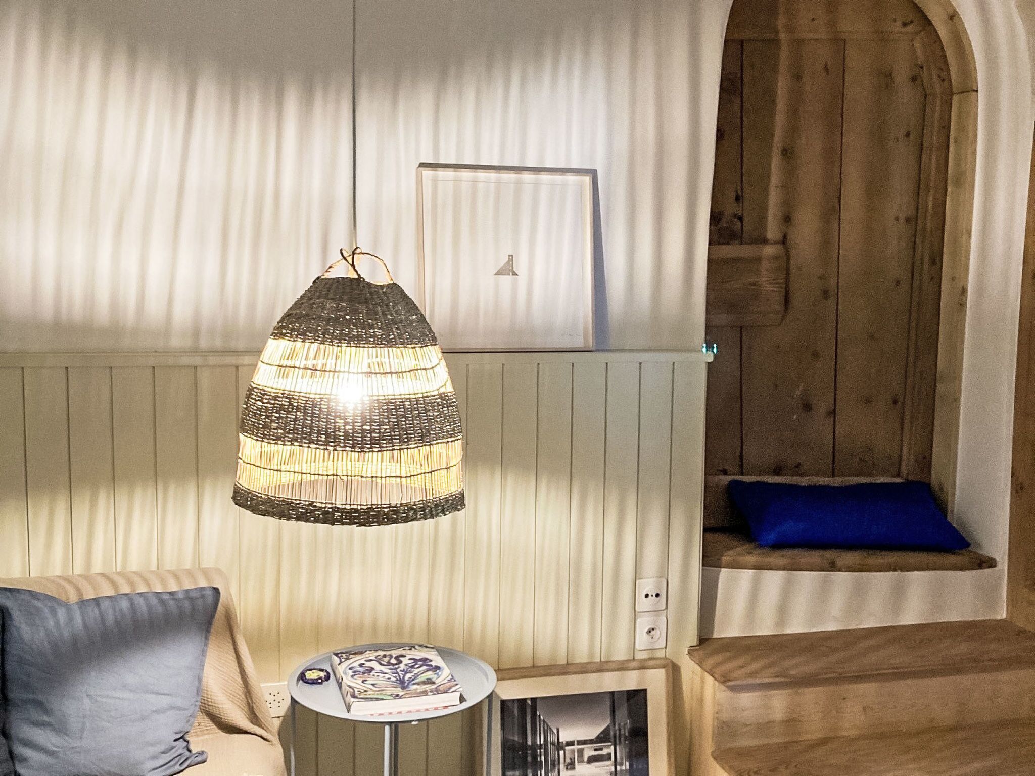 Ein Zimmer mit einer Pendelleuchte, einem kleinen Tisch mit einer Dekoration, einem blauen Kissen und einer Holzbank.
