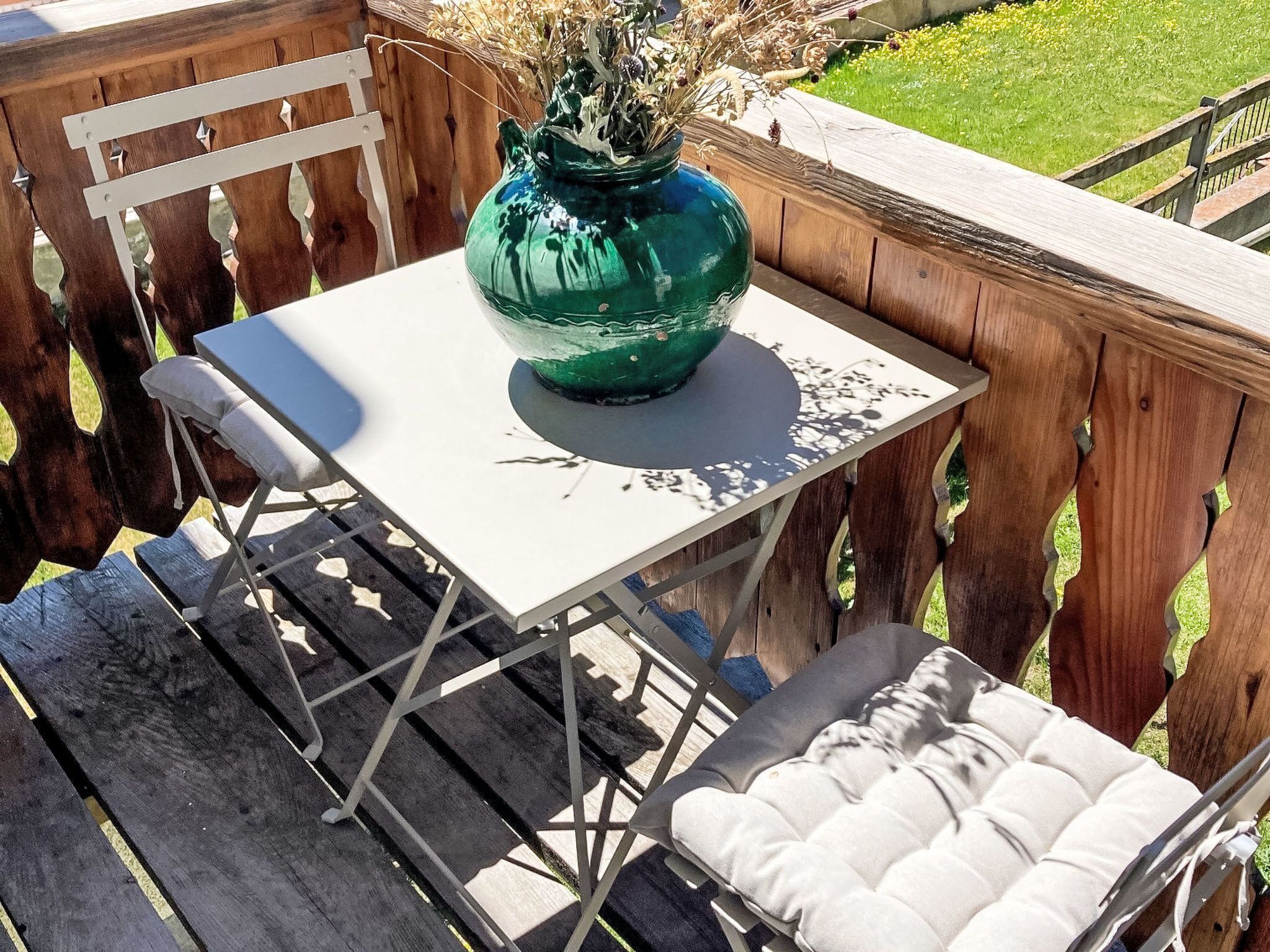 Eine Holzterrasse mit einem weißen Metalltisch und einem gepolsterten Stuhl.
