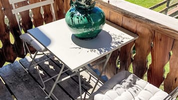 Eine Holzterrasse mit einem weißen Metalltisch und einem gepolsterten Stuhl.
