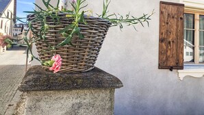 A wicker basket with plants on a stone pedestal against a building wall. - Chesa alb sco'l floc by Interhome (S-chanf)