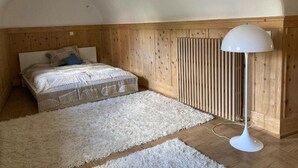 A bedroom with a bed, a white fluffy rug, a white floor lamp, and wooden paneling on the walls. - Chesa alb sco'l floc by Interhome (S-chanf)