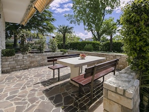 An outdoor patio with a stone floor, a table with a bowl of fruit, and wooden benches.
