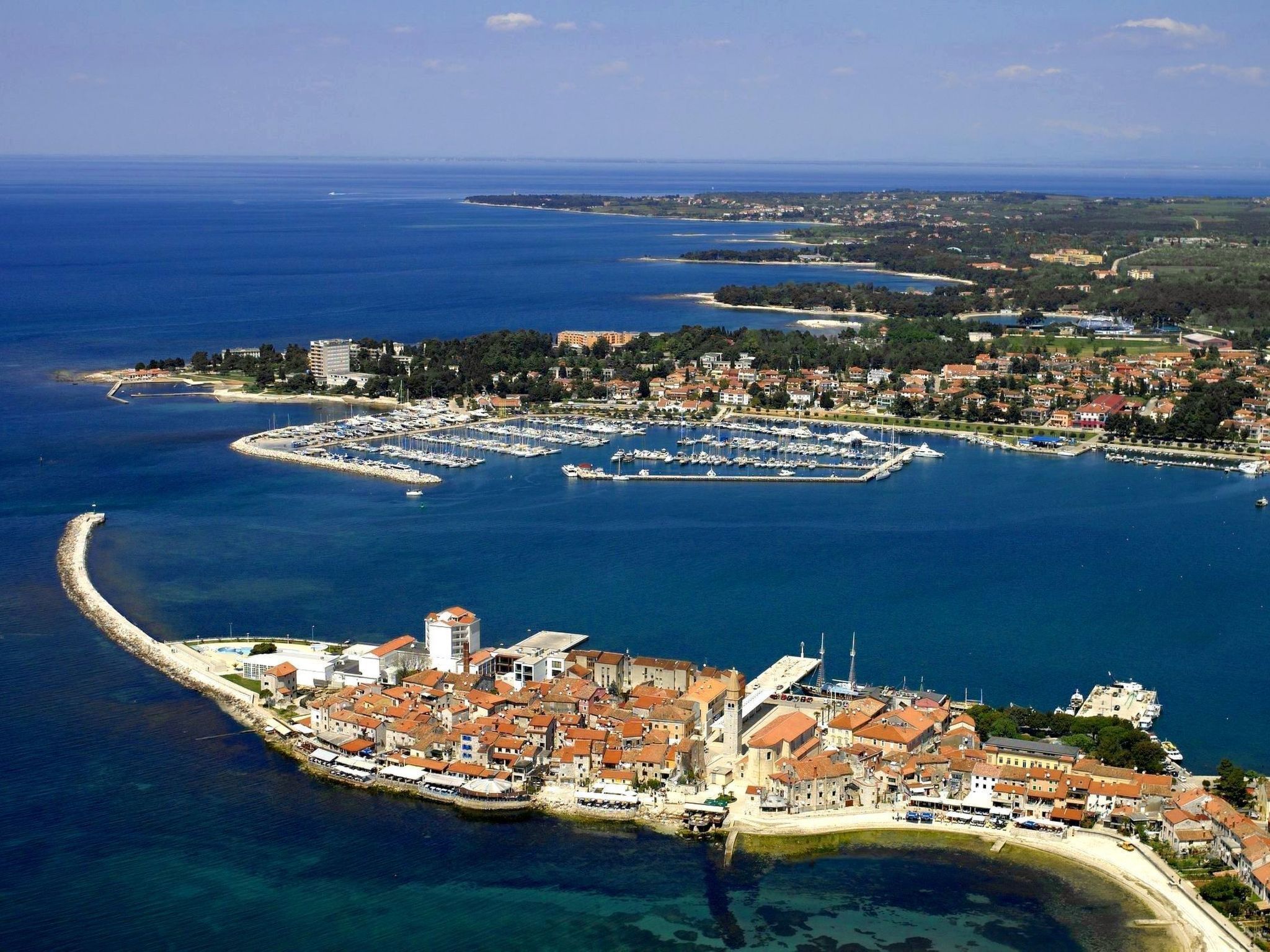 Vue aérienne d’une ville côtière avec un port de plaisance, des bâtiments historiques et une plage.