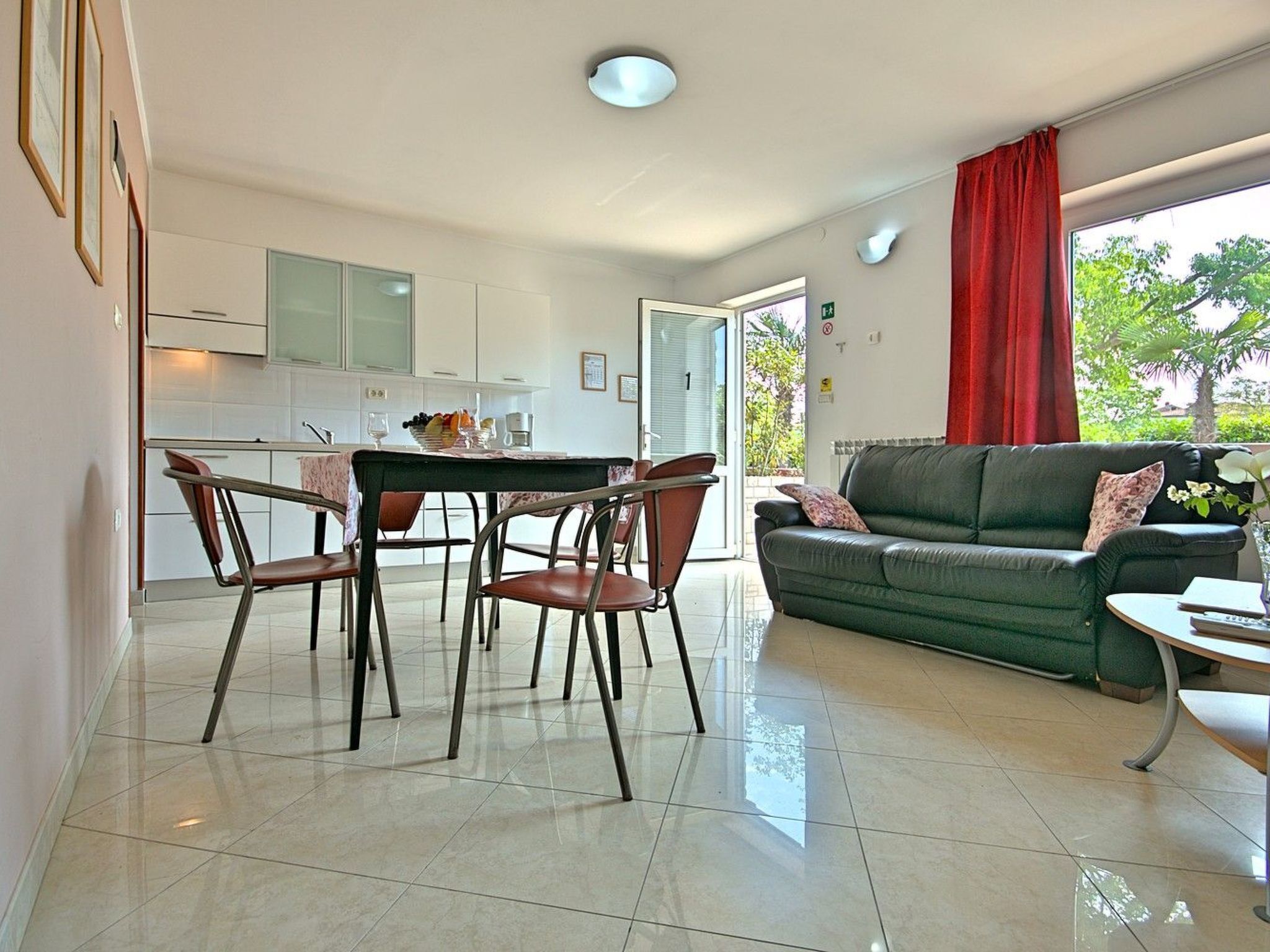 A modern living room with a green sofa, a dining table with chairs, and a kitchen area with white cabinets.