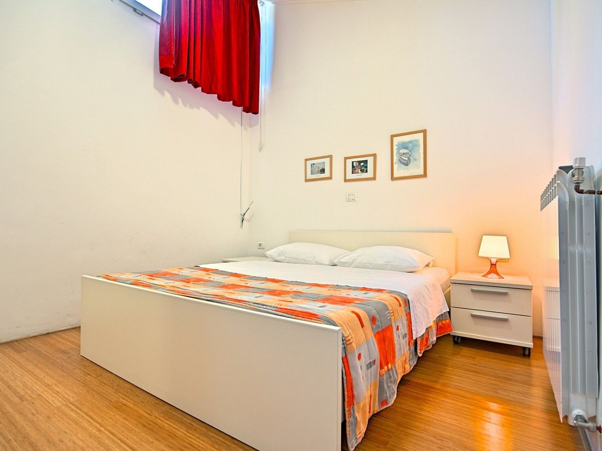 Ein Schlafzimmer mit Bett, Nachttisch, Lampe und Heizkörper.