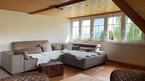 Een gezellige woonkamer met een modulaire bank, een houten tafel en een groot raam met uitzicht op de omgeving.