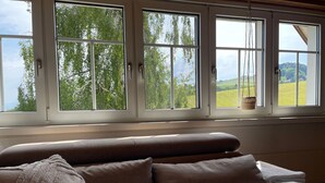 Een slaapkamer met een groot raam, een bed met een witte deken en uitzicht op een groen landschap.
