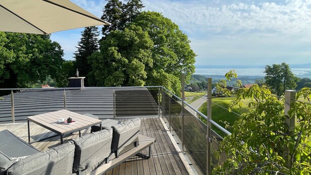 Een terras met buitenmeubilair, een pergola en uitzicht op een meer en heuvels.