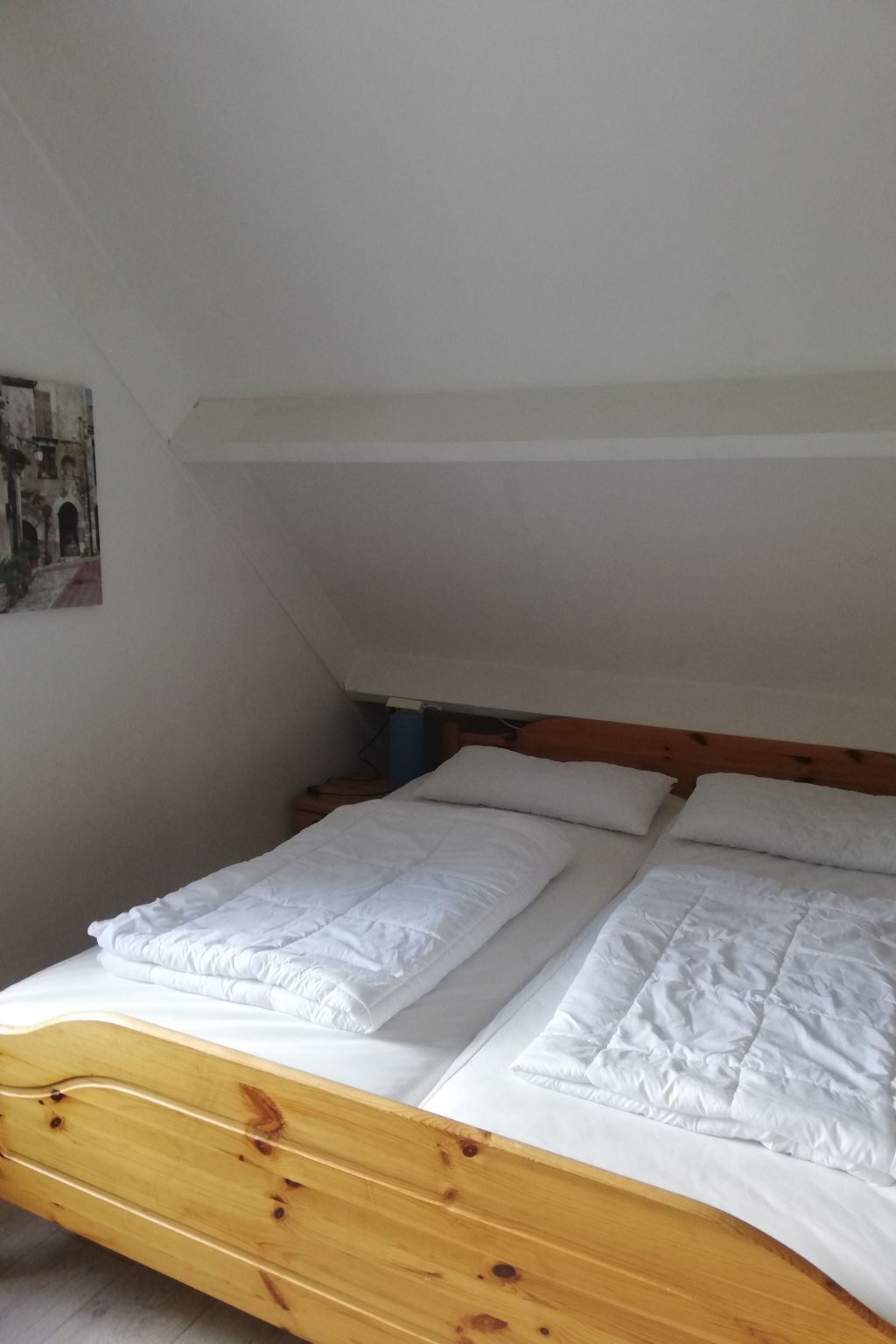 A single bed with white bedding in a room with white walls and a sloped ceiling.