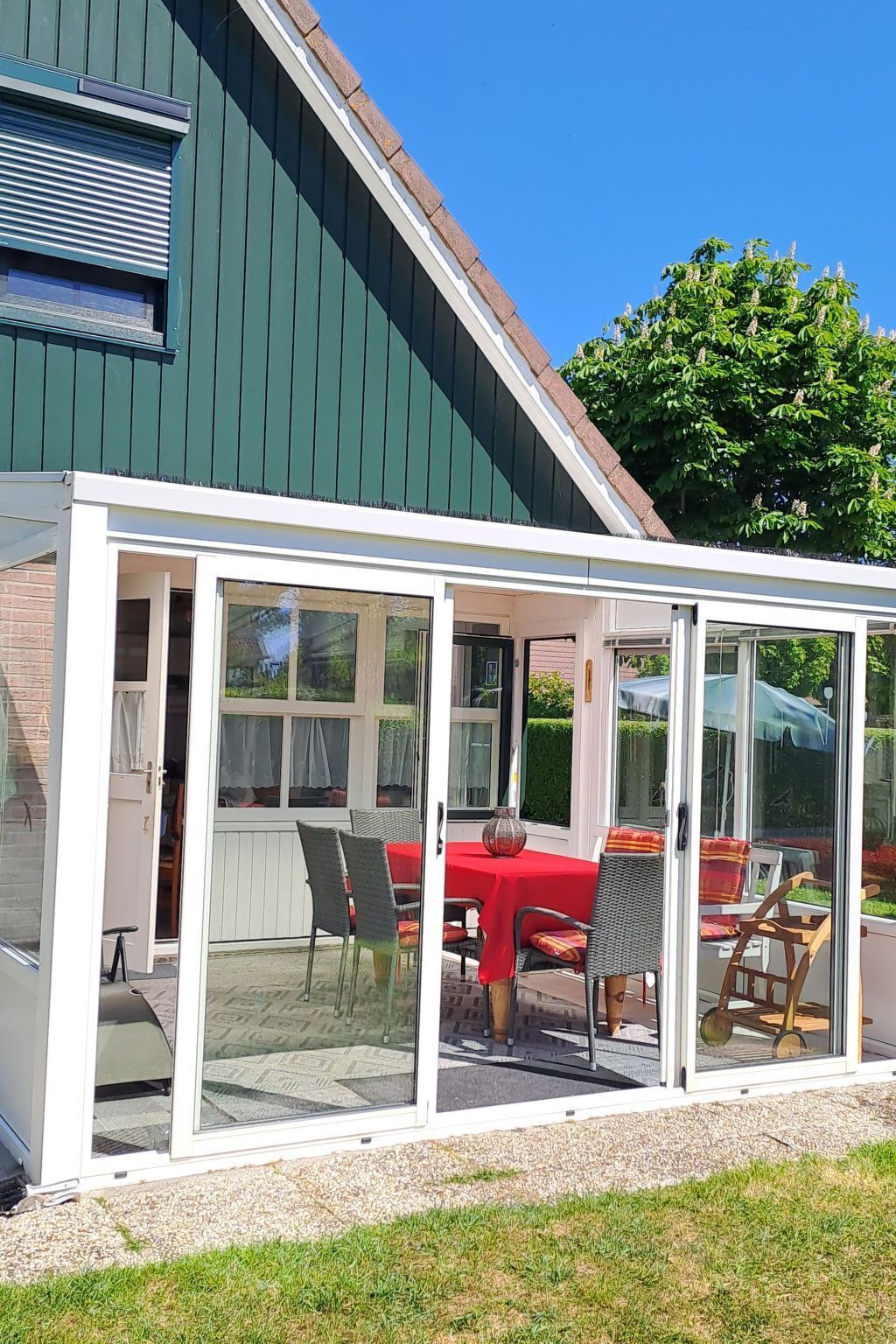 A conservatory with a glass enclosure, a red table, and wicker chairs.