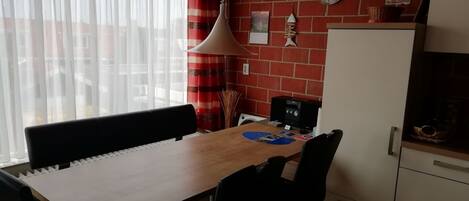 Une cuisine avec une table en bois, des chaises noires, un luminaire suspendu, une horloge et un mur en briques.