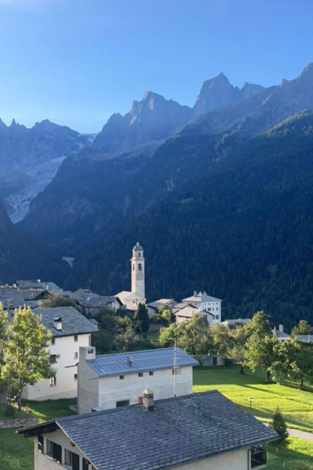 A mountainous village with a prominent church tower, surrounded by lush greenery and residential buildings.