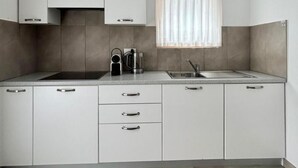 Een moderne keuken met witte kasten, een inbouwoven en een raam met transparante gordijnen.