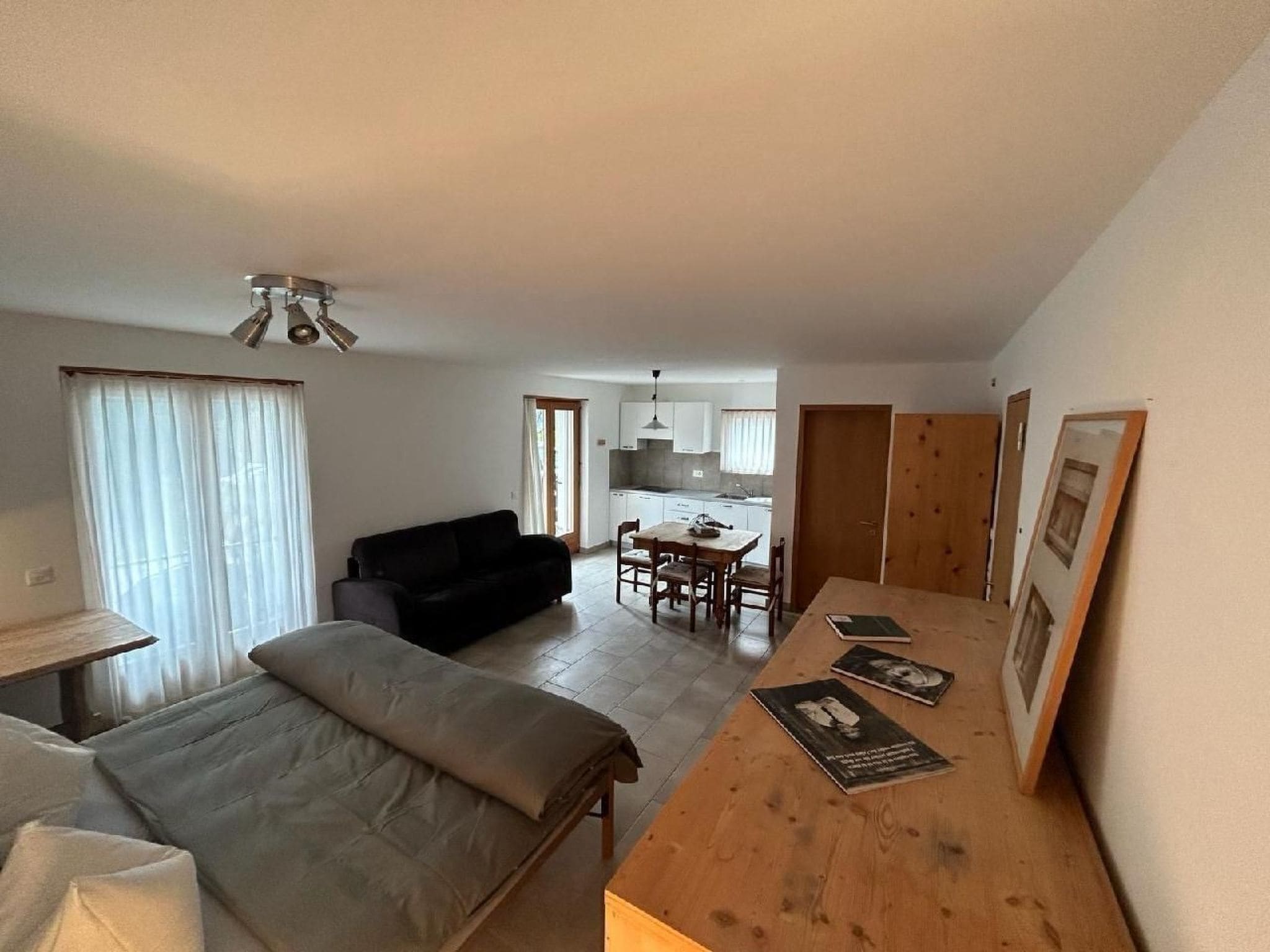 Ein kompakter Wohnbereich mit Bett, Sofa, Esstisch mit Stühlen und einer kleinen Küchenzeile im Hintergrund.