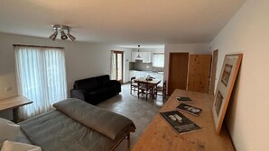 Een compacte leefruimte met een bed, een slaapbank, een eettafel met stoelen en een kitchenette op de achtergrond.