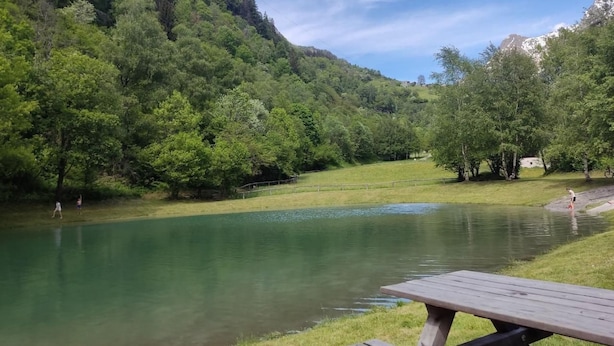 A picnic table by a calm river surrounded by lush greenery and hills. - in Borgonovo by Interhome (Borgonovo)