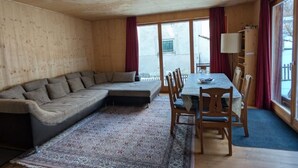 A cozy room with a wooden ceiling, a sofa, a dining table with chairs, and a large window with curtains. - in Borgonovo by Interhome (Borgonovo)