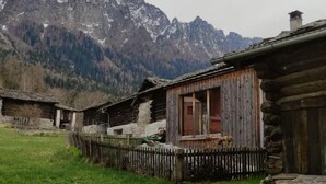A rustic log cabin with a wooden porch and a stone foundation, surrounded by a grassy yard and a mountain backdrop. - in Borgonovo by Interhome (Borgonovo)