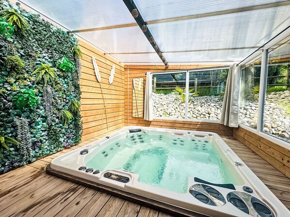 A hot tub in a wooden room with a glass ceiling, surrounded by a wall of plants.
