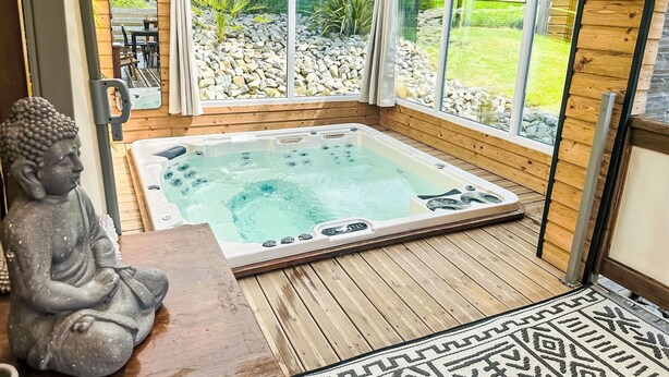 Ein Whirlpool in einem Holzraum mit großen Fenstern, einer Buddha-Statue und einem gemusterten Teppich.