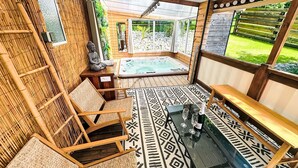 Ein überdachter Außenbereich mit Whirlpool, Sitzgelegenheiten und Blick auf einen Garten.