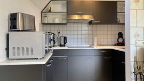 Een moderne keuken met donkere kastjes, een inbouwmagnetron, een koffiezetapparaat en een gasfornuis.