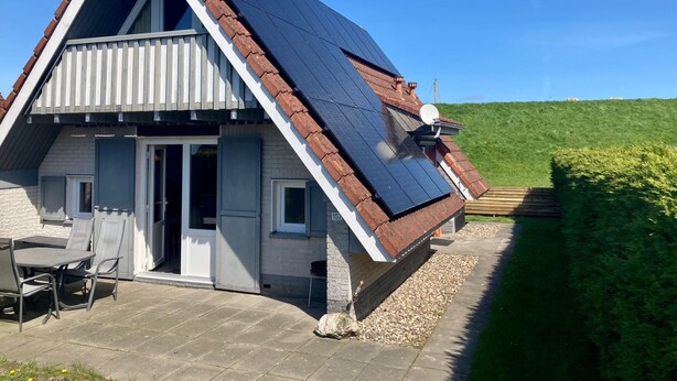 Een huis met een schuin dak, zonnepanelen en een schotelantenne.