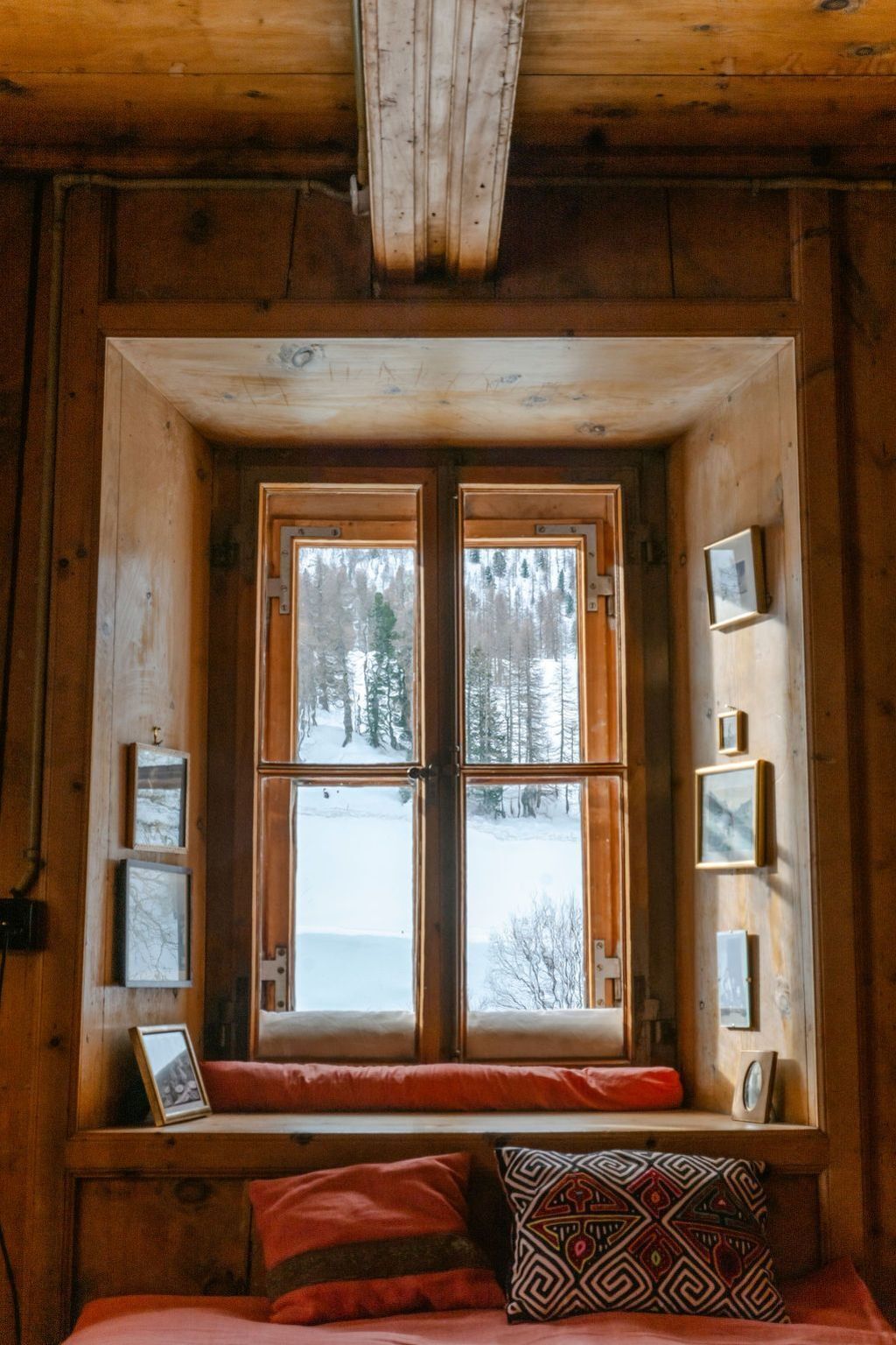 Ein Blockhauszimmer mit großem Fenster, Holzwänden, einer Bank und gerahmten Bildern.