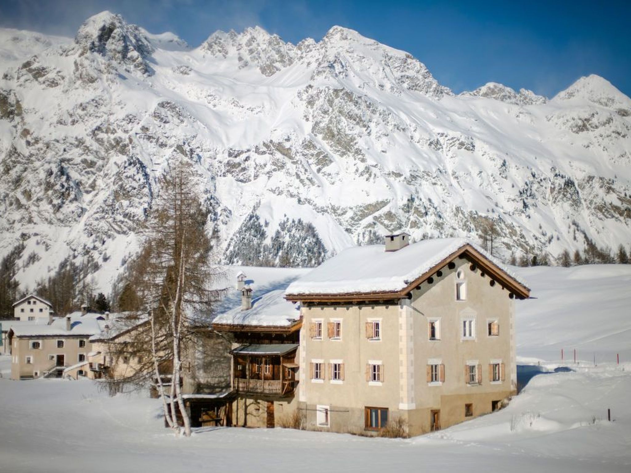 Eine verschneite Berglandschaft mit einem traditionellen Chalet mit zahlreichen Fenstern und einem Balkon.