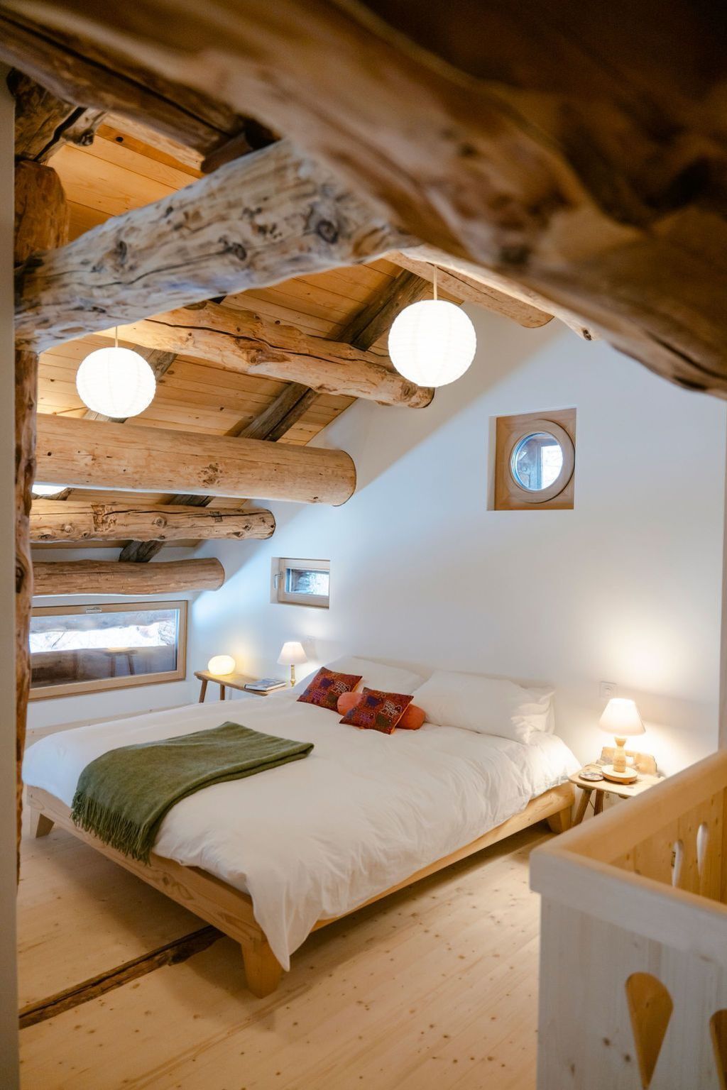 Une chambre confortable avec un plafond en bois, un lit recouvert de draps blancs, deux lampes de chevet et une fenêtre donnant sur un beau paysage.
