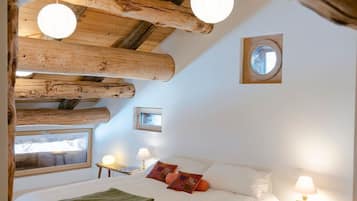 Ein gemütliches Schlafzimmer mit Holzbalkendecke, einem Bett mit weißen Leinentextilien, zwei Nachttischlampen und einem Fenster mit Blick.
